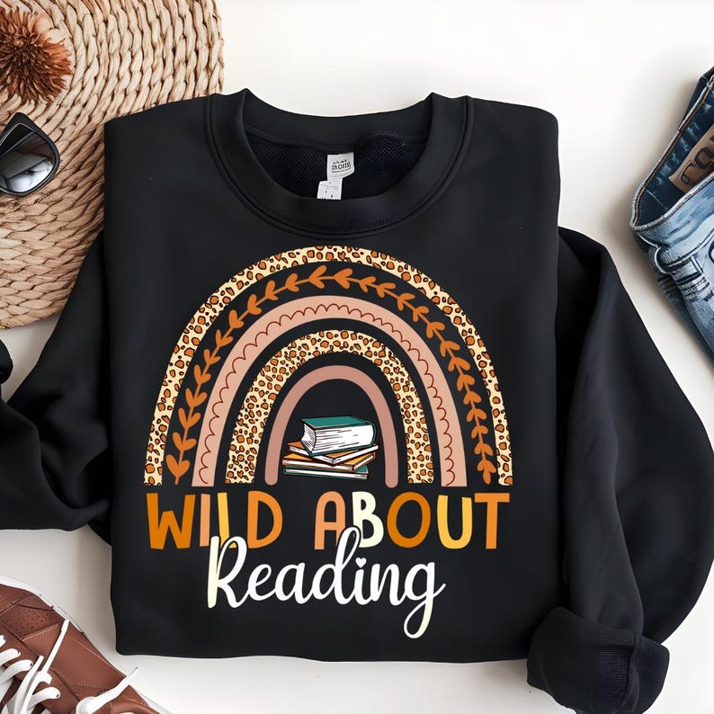 May include: Black sweatshirt with a rainbow design featuring a leopard print and a stack of books. The text "Wild About Reading" is printed below the rainbow.