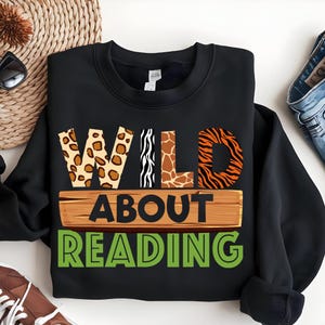 May include: Black sweatshirt with the text "WILD ABOUT READING" in green letters. The word "WILD" is made up of animal print letters: leopard, zebra, giraffe, and tiger.