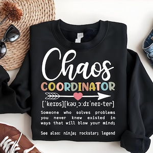Może przedstawiać: Czarny sweter z napisem "Chaos Coordinator" w kolorach tęczy i definicją tego terminu. Definicja brzmi: "['keips] [kǝu, ɔ:dı'ner-ter] Ktoś, kto rozwiązuje problemy, o kt&oacute;rych nigdy nie wiedziałeś, że istnieją, w spos&oacute;b, kt&oacute;ry rozsadzi ci m&oacute;zg; Zobacz także: ninja; rockstar; legenda"
