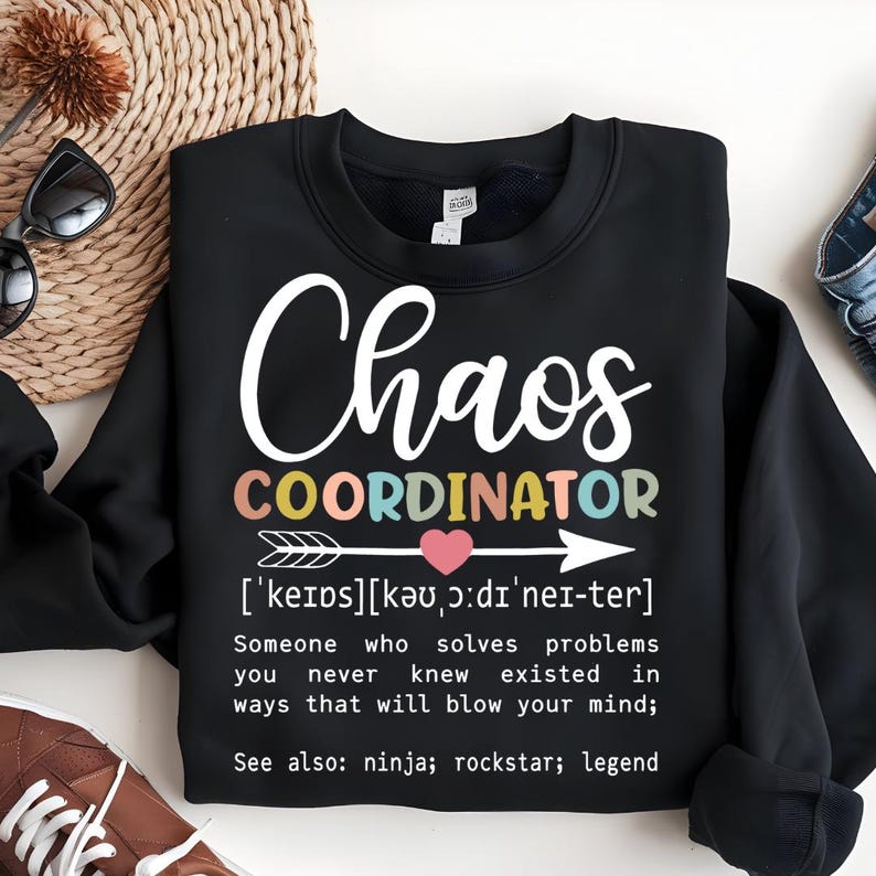 Może przedstawiać: Czarny sweter z napisem "Chaos Coordinator" w kolorach tęczy i definicją tego terminu. Definicja brzmi: "['keips] [kǝu, ɔ:dı'ner-ter] Ktoś, kto rozwiązuje problemy, o kt&oacute;rych nigdy nie wiedziałeś, że istnieją, w spos&oacute;b, kt&oacute;ry rozsadzi ci m&oacute;zg; Zobacz także: ninja; rockstar; legenda"