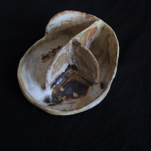 May include: A handmade ceramic divided dish with an unusual, organic shape. The dish has three compartments and is finished in a neutral colour palette with brown and green accents. Ideal for serving snacks or small portions.
