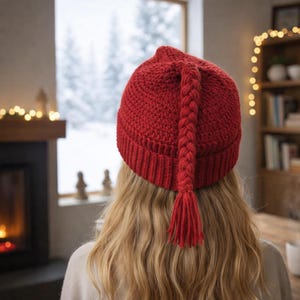 以下が含まれることがあります： 長い三つ編みのタッセルが付いた赤いニット帽。帽子は無地の赤色で、リブ編みのつばが付いています。タッセルは帽子の後ろに垂れ下がっています。この帽子はおそらく手作りで、冬の着用に適しています。