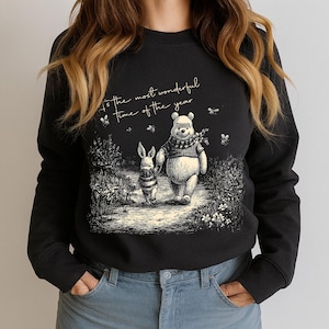 May include: Black sweatshirt featuring a Winnie the Pooh illustration with Piglet. The image shows the characters walking on a path with the text "It's the most wonderful time of the year". The design includes bees and floral elements.
