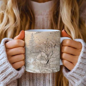 May include: White ceramic mug featuring a winter landscape design. The design includes trees, birds, and a snowy scene in shades of beige, gray, and white. The mug has a white handle and is held by a person wearing a cream-colored sweater.