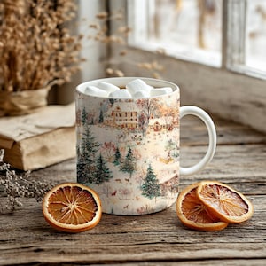 Puede incluir: Una taza de cer&aacute;mica blanca llena de malvaviscos, con una escena de paisaje invernal con casas y &aacute;rboles. Dos rodajas de naranja secas se encuentran junto a la taza sobre una superficie de madera, creando un tema estacional.