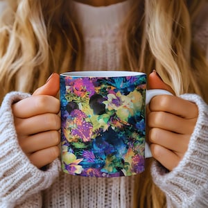 May include: A ceramic mug featuring a vibrant, abstract floral pattern in shades of deep purple, bright magenta, electric blue, and lime green. The design covers the exterior surface, while the handle and interior remain solid white.