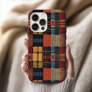 May include: A colorful phone case with a patchwork design. The case features a mix of red, orange, yellow, blue, and green squares, creating a textured, woven appearance. The case is designed to fit a smartphone with multiple camera lenses.