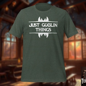 May include: A dark green t-shirt with the text "Just Goblin Things" in white lettering. The text is surrounded by a white graphic of a goblin-like creature with fangs.