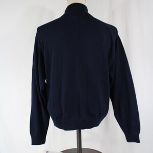 May include: A solid navy blue long-sleeve sweater featuring a mock neck collar, ribbed cuffs, and a ribbed hemline. The garment is displayed on a mannequin torso, showcasing a simple, plain back view of the knit pullover design.