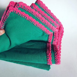 May include: Stack of green fabric napkins with pink crocheted trim.