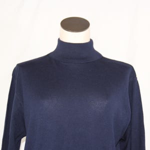 May include: A solid navy blue long-sleeve sweater featuring a high mock turtleneck collar. The garment is constructed from a smooth, fine-knit fabric with a consistent dark blue color throughout the torso and sleeves, displayed on a mannequin.