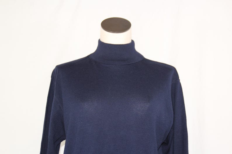 May include: A solid navy blue long-sleeve sweater featuring a high mock turtleneck collar. The garment is constructed from a smooth, fine-knit fabric with a consistent dark blue color throughout the torso and sleeves, displayed on a mannequin.