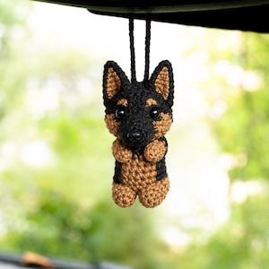 Può includere: Un piccolo ornamento all'uncinetto fatto a mano a forma di cane pastore tedesco. La figura presenta filato nero e marrone, orecchie a punta, due occhi in plastica nera e un naso nero. Un cappio di filo nero è fissato sulla parte superiore.