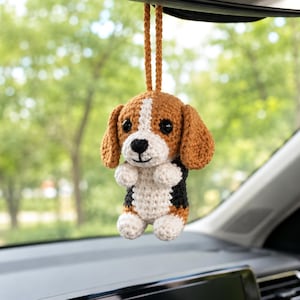 Puede incluir: Un adorno de perro beagle tejido a ganchillo que cuelga de un lazo de hilo marrón. El perro presenta hilo marrón, blanco y negro, con ojos de plástico negro y una nariz y boca bordadas. La figura tiene orejas caídas y es para colgar.