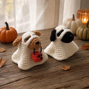 Peut inclure: Deux figurines de chiens au crochet déguisées en fantômes. L'un est un chien marron tenant un petit seau citrouille orange, l'autre est un chien noir et blanc. Tous deux portent des costumes de fantômes blancs au crochet avec des ouvertures.