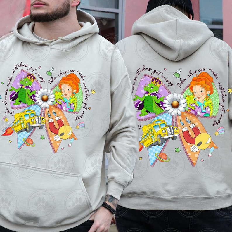 May include: A light gray hoodie featuring a colorful graphic design. The design includes a yellow school bus, a daisy, and cartoon characters. Text on the hoodie reads "Take chances make mistakes get messy."