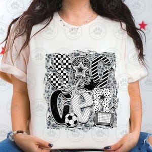 Puede incluir: Camiseta blanca con un dise&ntilde;o gr&aacute;fico en blanco y negro de la palabra "Soccer" con un bal&oacute;n de f&uacute;tbol, estrellas y un patr&oacute;n a cuadros.