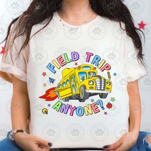 May include: White t-shirt featuring a colourful graphic of a yellow school bus with the text "Field Trip Anyone?"