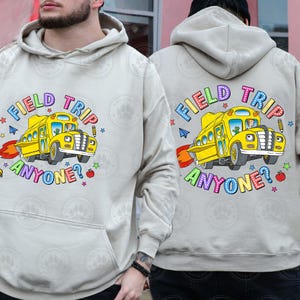 May include: A light grey hoodie featuring a yellow school bus graphic and the text "Field Trip Anyone?" in rainbow lettering. The hoodie has a hood and a pouch pocket.