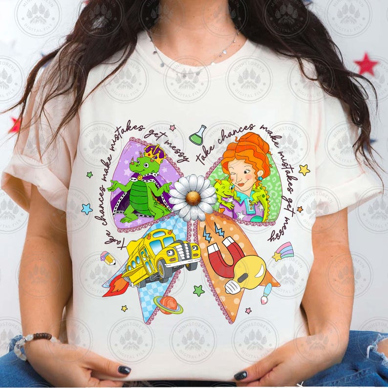 May include: A cream-colored t-shirt featuring a colorful bow design with the text "Take chances make mistakes get messy." The bow includes illustrations of a school bus, a dragon, a woman with red hair, and other whimsical elements.