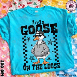 Op de afbeelding: Een turquoise blauw t-shirt met een afbeelding van een gans met een zonnebril, een grijze hoodie en een zwarte pet. De tekst "dada GOOSE ON THE LOOSE" staat boven en onder de ganzenillustratie. Zwart-wit geblokte randen en sterren zijn ook aanwezig.