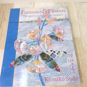 May include: A book titled "Fantasies & Flowers Origami in Fabric for Quilters" by Kumiko Sudo. The cover shows a floral design with pink, orange, and blue origami flowers on a blue and white background.