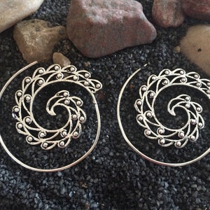 May include: A pair of silver hoop earrings with a spiral design. The earrings are made of metal and have a delicate, intricate design.