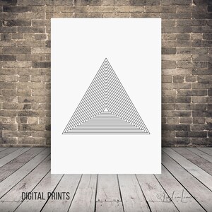 May include: A white print featuring a black geometric triangle design composed of concentric lines. The words "DIGITAL PRINTS" are printed at the bottom left corner. The print is displayed against a brick wall and wooden floor.