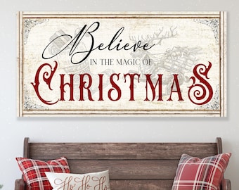 May include: A rectangular wall sign with a distressed cream background featuring the black script text Believe and the red decorative text CHRISTMAS, with the words IN THE MAGIC OF in black, and a faint line drawing of a reindeer-drawn sleigh.