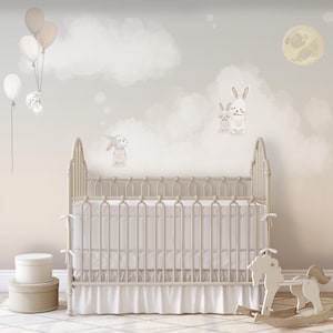 Könnte beinhalten: Ein weißes Babybett mit einem weißen und grauen gemusterten Bettrock, einem Schaukelpferd und einem weißen Aufbewahrungskorb. Die Wand hinter dem Babybett ist hellgrau gestrichen und zeigt ein Wandbild mit Wolken, einem Mond und Hasen.