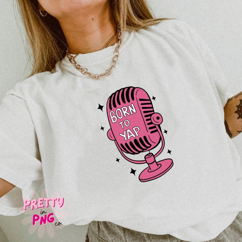 以下が含まれることがあります： ピンクのマイクのグラフィックと「Born to Yap」というテキストが書かれた白いTシャツです。