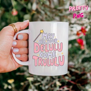 Pode incluir: Caneca de cer&acirc;mica branca com um design rosa e roxo que diz "May all your Delulu come Trululu" com um gr&aacute;fico de estrela amarela e varinha.