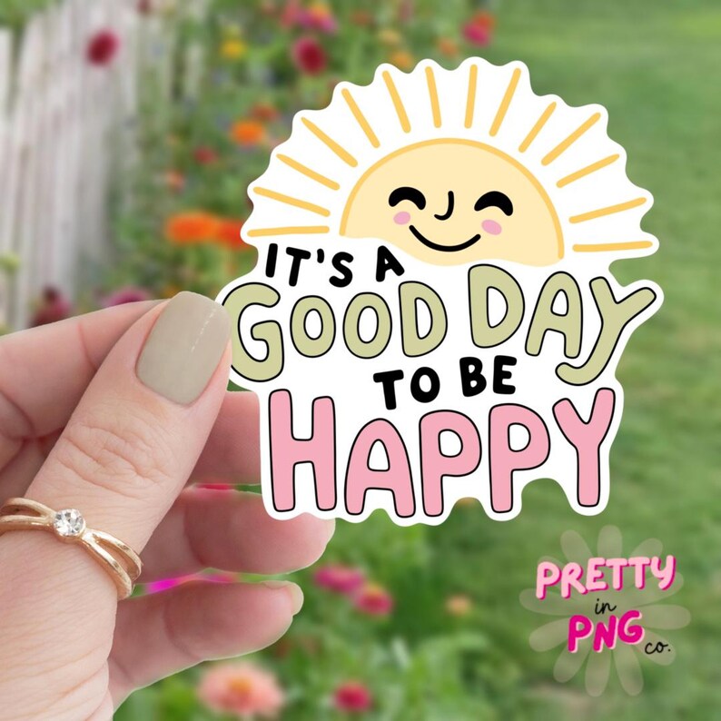 May include: A sticker with a smiling sun and the text "It's a good day to be happy" in black, green, and pink. The sticker has a white border and the words "Pretty in PNG co." in pink.