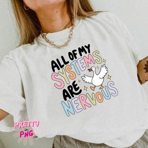 Puede incluir: Camiseta blanca con un dise&ntilde;o gr&aacute;fico colorido que dice "All of my systems are nervous" con una ilustraci&oacute;n de ganso de dibujos animados.
