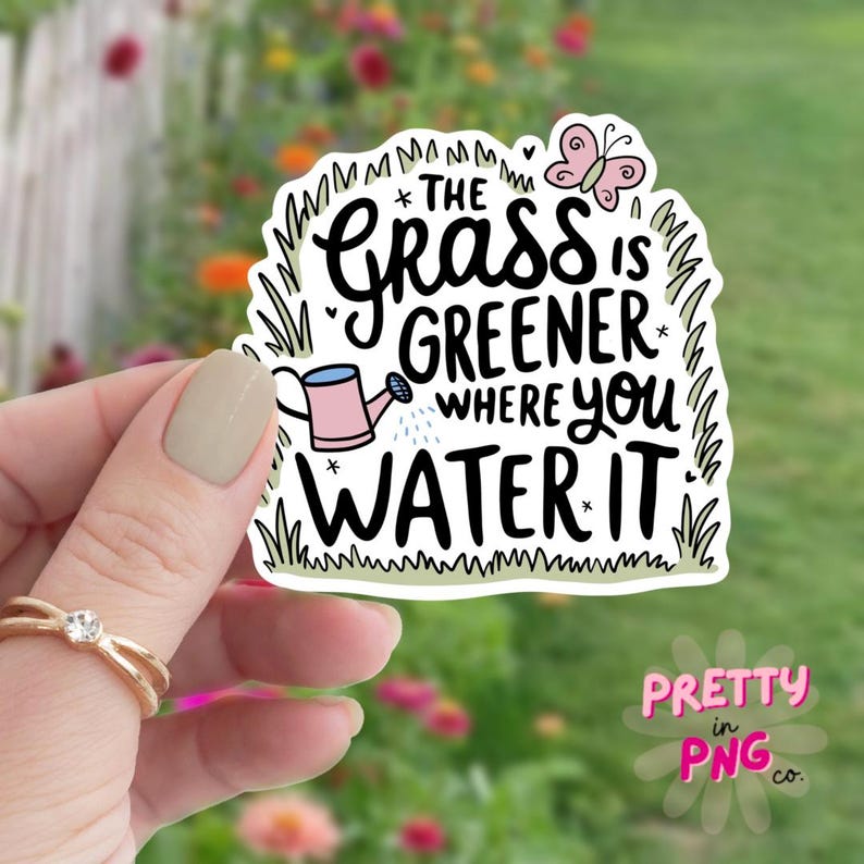 May include: A white sticker with a green grass border and a pink butterfly. The sticker features the text "*THE GRASS IS GREENER WHERE you WATER IT*" with a pink watering can and a white star.