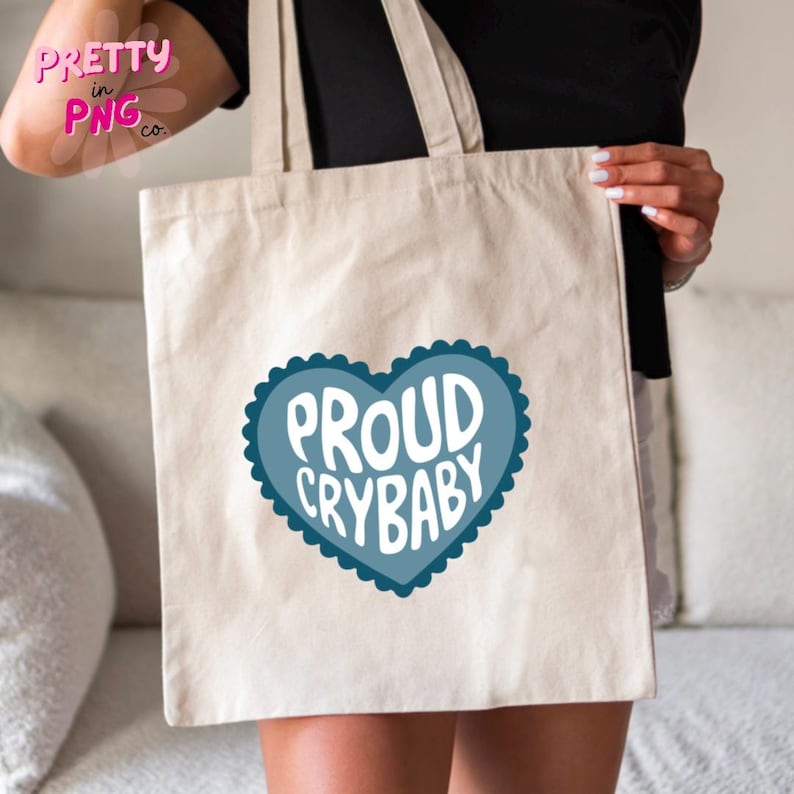 May include: A white canvas tote bag with a blue heart design that says "Proud Crybaby" in white text.