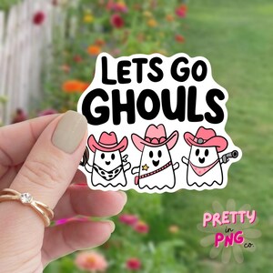 Pode incluir: Um adesivo branco com tr&ecirc;s fantasmas de desenho animado usando chap&eacute;us de caub&oacute;i rosa e o texto "Lets Go Ghouls".