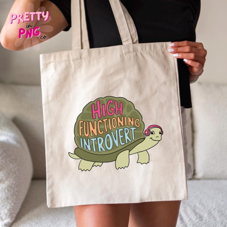 May include: A white canvas tote bag with a green turtle wearing pink headphones and the text "HIGH FUNCTIONING INTROVERT" in colorful letters.
