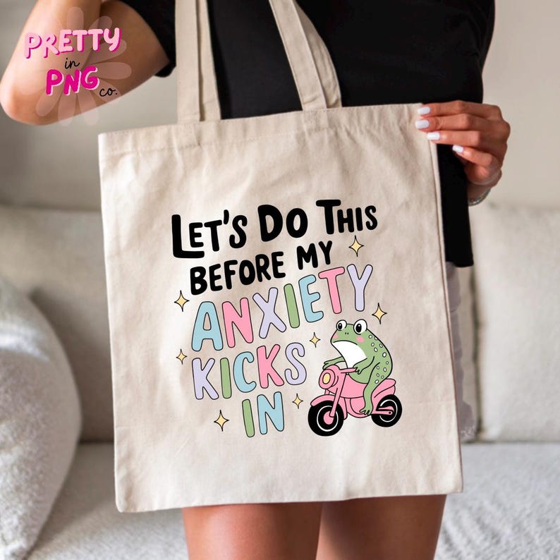 K&ouml;nnte beinhalten: Eine wei&szlig;e Canvas-Tragetasche mit dem Text "Let's do this before my anxiety kicks in" in Schwarz. Darunter befindet sich ein Cartoon-Frosch, der ein rosa Motorrad f&auml;hrt.
