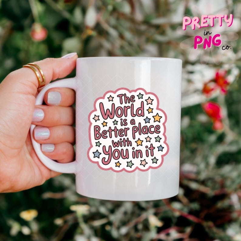 Peut inclure: Mug en c&eacute;ramique blanche avec un motif rose et blanc qui dit "The World is a Better Place with You in it." La tasse est tenue par une main avec des bagues dor&eacute;es. La tasse a une grande anse.