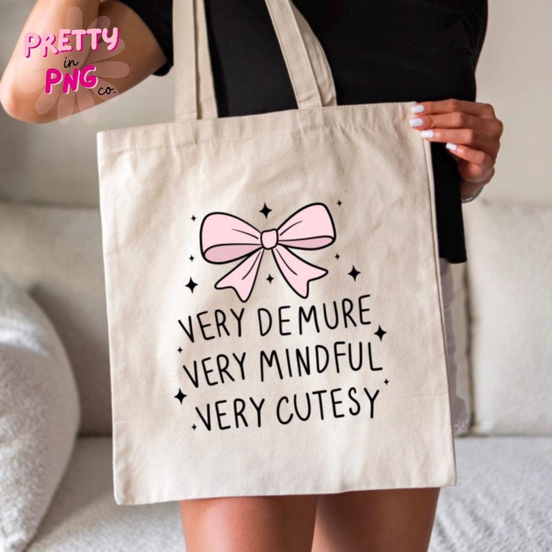 May include: A white canvas tote bag with a pink bow and the text "Very Demure, Very Mindful, Very Cutesy".
