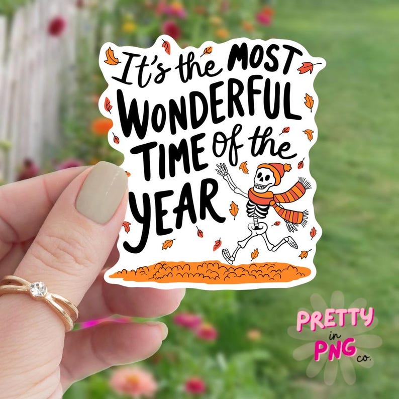 May include: White sticker with the text "It's the most wonderful time of the year" in black. A cartoon skeleton wearing a red and orange hat and scarf is running through a pile of orange leaves.
