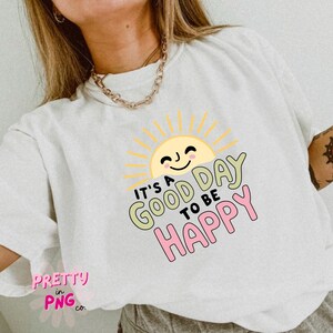 May include: White t-shirt with a smiling sun graphic and the text "IT'S A GOOD DAY TO BE HAPPY" in pastel colors. The shirt also has the text "PRETTY in PNG co." in pink.