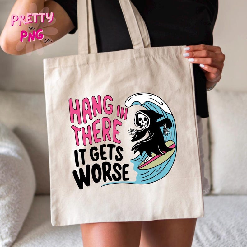 May include: Beige tote bag featuring the text "HANG IN THERE IT GETS WORSE" in pink and black. A cartoon grim reaper surfs a wave. The bag has long handles and a simple design.
