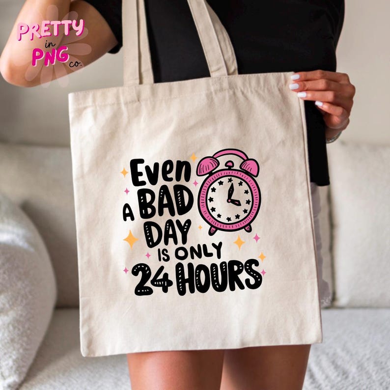 May include: A white tote bag with a pink alarm clock graphic and the text "Even a bad day is only 24 hours".