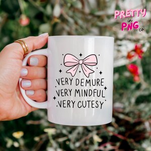 May include: White ceramic mug with a pink bow and the text "Very Demure, Very Mindful, Very Cutesy" printed on it.