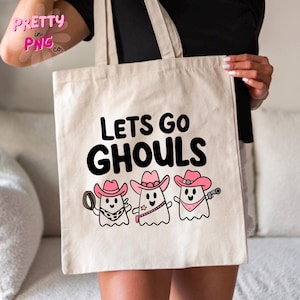 Pode incluir: Uma bolsa tote branca com o texto "Lets Go Ghouls" em preto. Abaixo do texto, h&aacute; tr&ecirc;s fantasmas de desenhos animados usando chap&eacute;us de caub&oacute;i rosa.