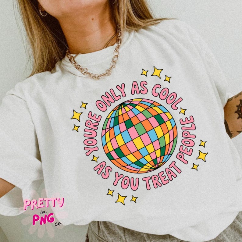 May include: White t-shirt with a colorful disco ball graphic and the text "YOU'RE ONLY AS COOL AS YOU TREAT PEOPLE." The design includes pink text and yellow stars. The shirt is a casual, comfortable style.