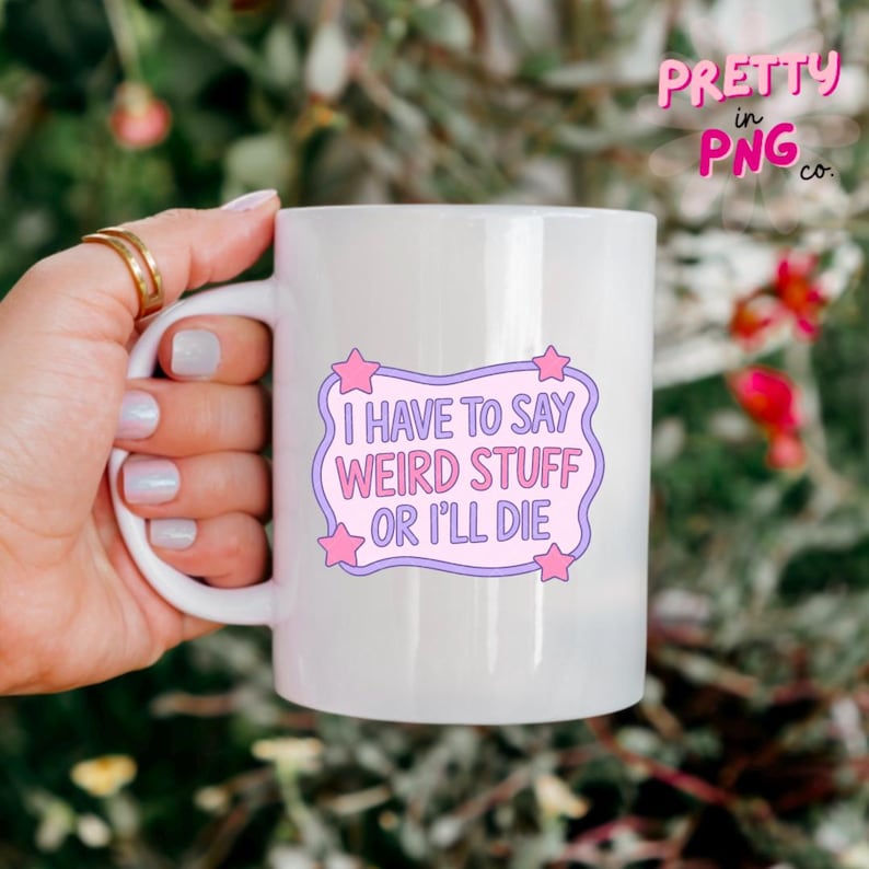 May include: White ceramic mug with the text "I HAVE TO SAY WEIRD STUFF OR I'LL DIE" in a purple and pink design. The mug has a curved handle and is held by a person. The mug is from Pretty in PNG co.