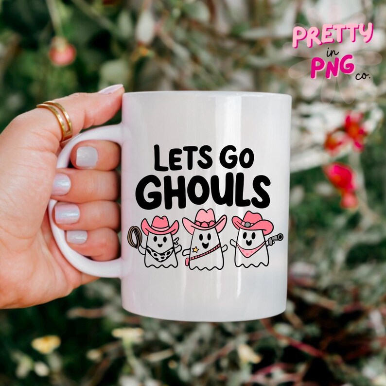 Pode incluir: Caneca de cer&acirc;mica branca com um gr&aacute;fico em preto e branco de tr&ecirc;s fantasmas usando chap&eacute;us de caub&oacute;i rosa. O texto "Lets Go Ghouls" &eacute; impresso em preto na caneca.